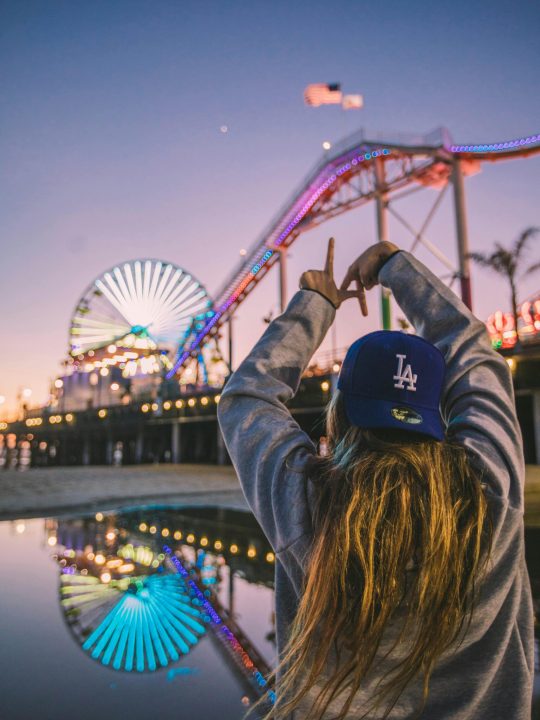 Back view of a woman enjoying Santa Monica Pier amusement park at twilight, reflecting vibrant lights.